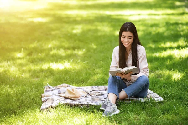 Розслабляється в парку. Дівчина читає книгу, сидячи на галявині — стокове фото