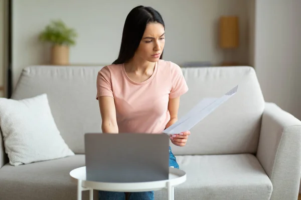 Znepokojená žena na notebooku drží účty sedí na pohovce vnitřní — Stock fotografie