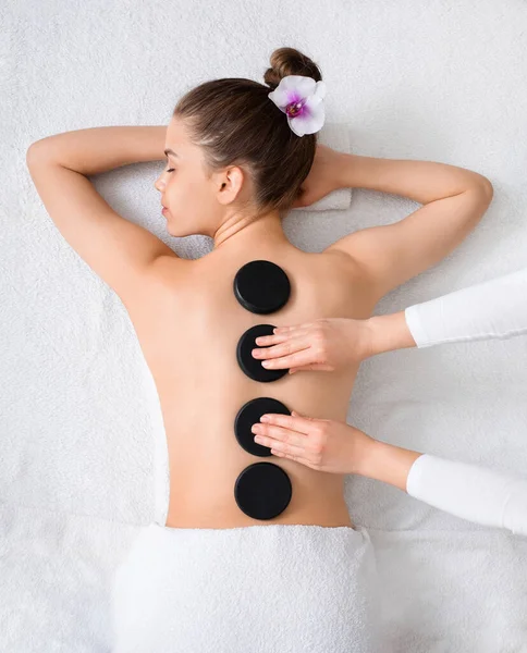 Ung kvinna som går på spa, får heta stenar massage — Stockfoto