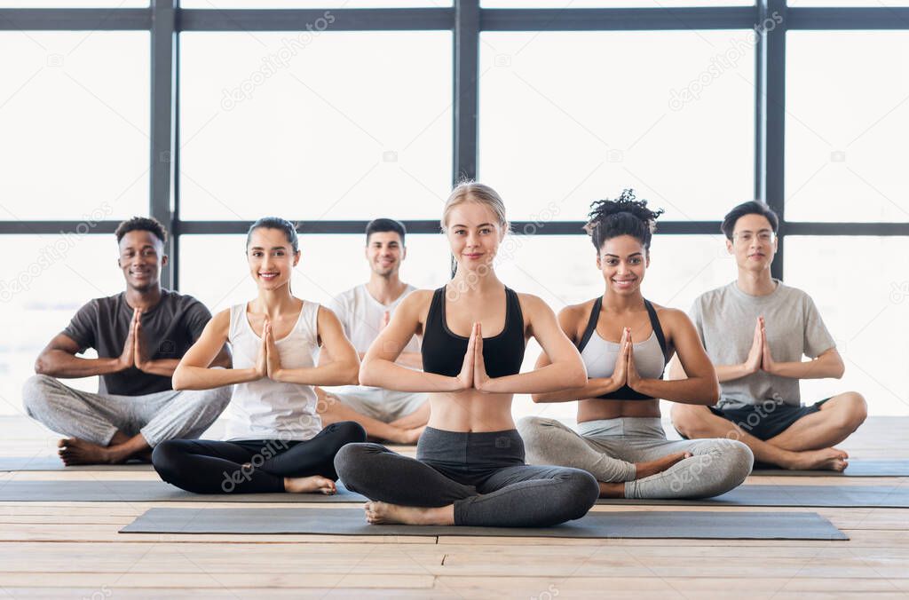 Namaste. Young sporty people practicing yoga in modern sport club