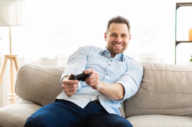 Genç adam kanepede oturmuş video oyunları oynuyor.