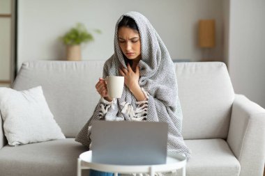 Hasta kız laptopta oturmuş çay içiyor. Evden çalışıyor.