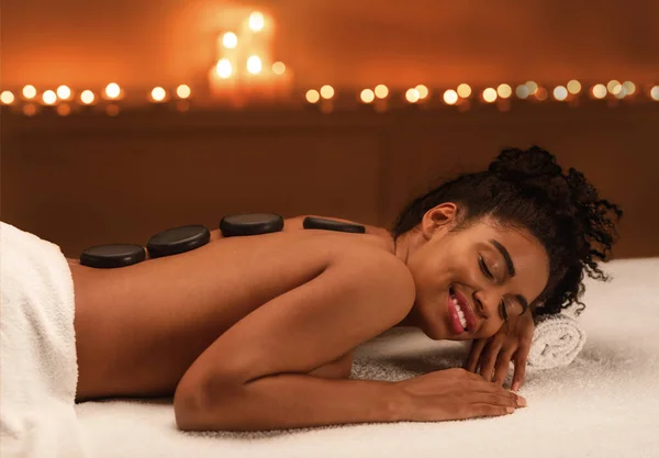 Relajada chica africana disfrutando de piedras calientes de masaje en el spa — Foto de Stock