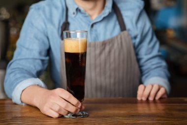 Köpüklü koyu bira. Barmen ahşap tezgahta bir bardak bira tutuyor.