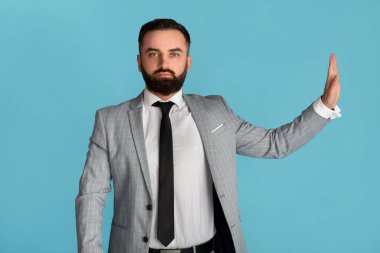 Ciddi bir ofis çalışanı, mavi arka planda inkârını belirterek dur hareketi gösteriyor.