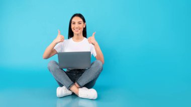 Dizüstü bilgisayarı olan mutlu bir bayan başparmak kaldırıyor.