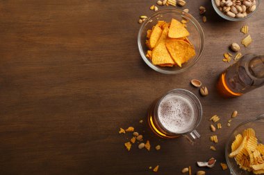 Bardaki müşteri masası. Bir bardak bira ve şişe, nacho, cips ve fıstık tabakta ve dağınık