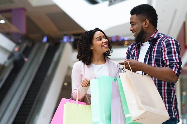 Feliz pareja africana pasando tiempo juntos en el centro comercial, sosteniendo bolsas de colores —  Fotos de Stock