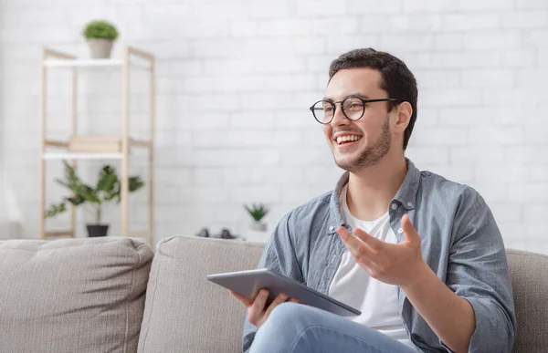 Blogger en el lugar de trabajo. riéndose chico en gafas con tableta en las manos explica algo — Foto de Stock