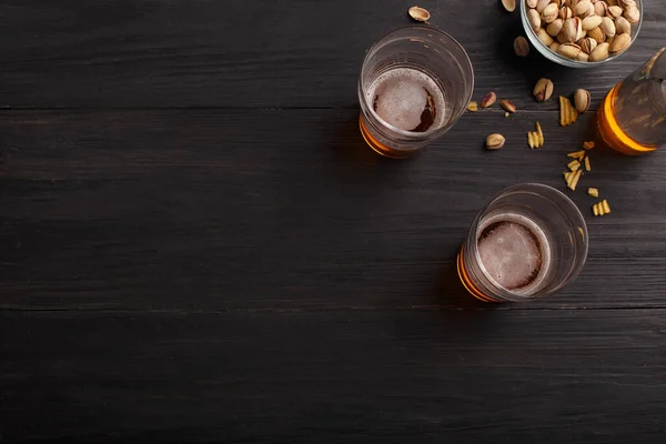 İki bardak bitmemiş bira ve şişe. Şam fıstığı, cips ve nachos cam tabaklarda ve dağınık — Stok fotoğraf