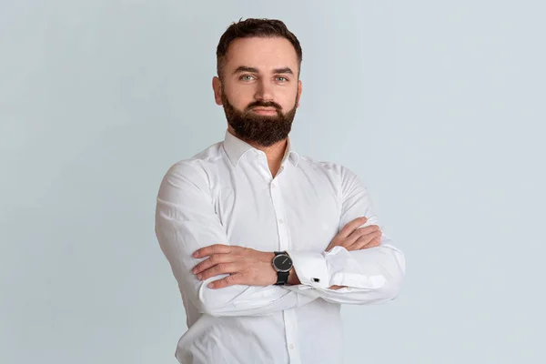 Attractive bearded CEO in white shirt standing with crossed arms on grey background — Stock Photo, Image