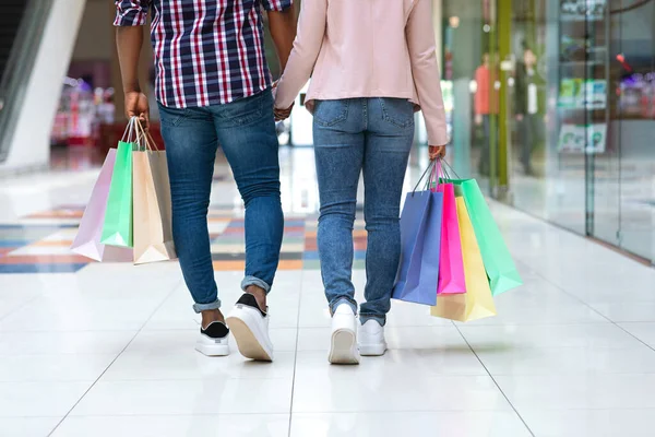 Pareja afroamericana joven con bolsas de compras caminando por el centro comercial cogidas de la mano, panorama, vista trasera, espacio para copiar — Foto de Stock