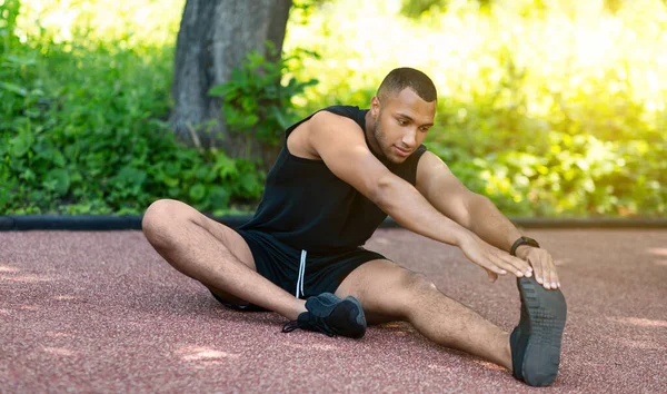 Africano desportista americano esticando as pernas na pista de jogging no parque — Fotografia de Stock