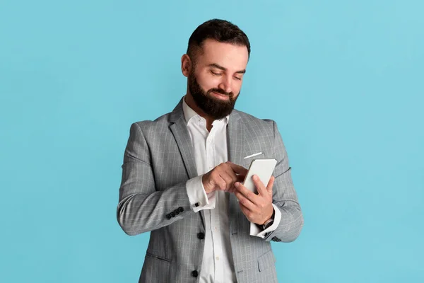 Schöner Firmenmitarbeiter, der auf dem Smartphone im Internet surft, blauer Hintergrund — Stockfoto