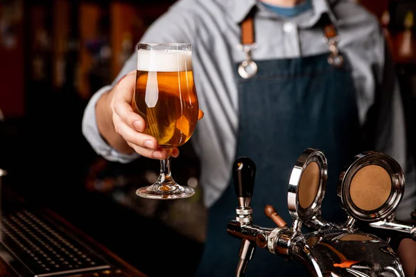 Bier vrijdagavond. Barman geeft glas licht bier met schuim in donker interieur — Stockfoto