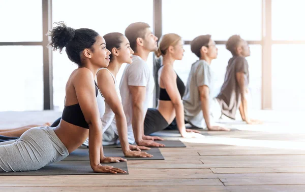 Yogagruppsmedlemmar som gör kobra poserar samtidigt som de övar i modern loftstudio — Stockfoto