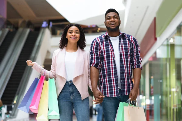 Pareja africana feliz disfrutando de compras en grandes almacenes, posando con bolsas de colores —  Fotos de Stock