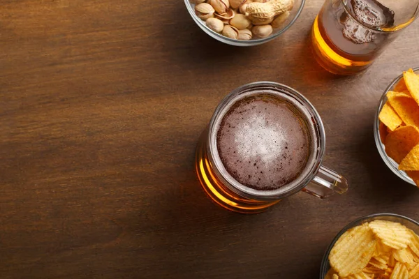 Кружка пива и бутылка с напитком, чипсы начос и фисташки в стеклянных тарелках — стоковое фото