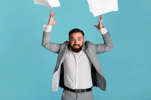 Zvládání pracovního stresu. Rozzlobený Millennial kancelář zaměstnanec házení papíry na modrém pozadí — Stock fotografie