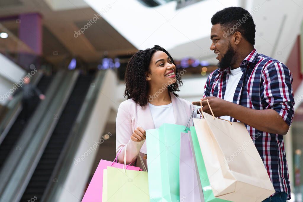 Happy african couple spending time together in shopping mall, holding colorful bags