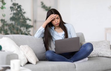 Bağımsız stres. Endişeli Asyalı kız işten sonra evde dizüstü bilgisayar başında yoruldu.