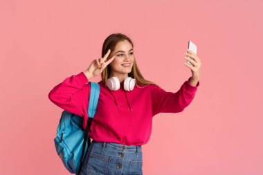 Sırt çantalı gülümseyen genç kız barış işareti yapıyor ve selfie çekiyor.