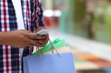 Nakit Kavramı. Alışveriş sırasında AVM 'de akıllı telefon kullanan alışveriş çantalı adam.