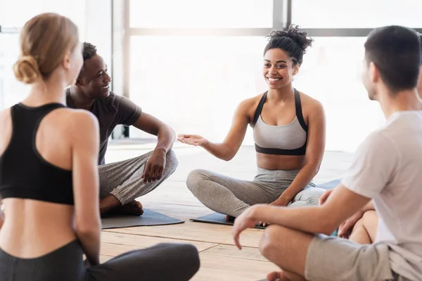 Инструктор по йоге чёрной женщины разговаривает с молодыми йогами после уроков. — стоковое фото