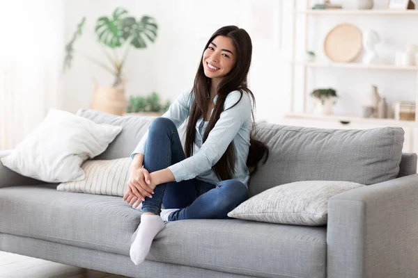 Thuis Comfort. mooi glimlachen aziatisch meisje poseren op sofa in woonkamer — Stockfoto