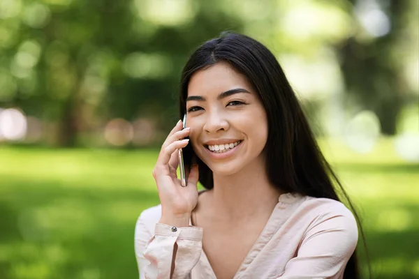 Porträtt av leende asiatiska flicka talar på mobiltelefon utomhus, Avslappnande i parken — Stockfoto