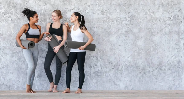 Pilates-Kurs. Sportliche junge Mädchen stehen mit Yogamatten an der grauen Wand — Stockfoto