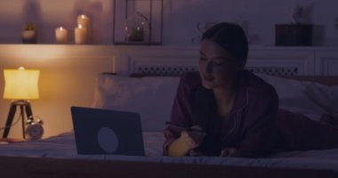 Kadın gazeteci dizüstü bilgisayarda geziniyor ve yatakta notlar alıyor.