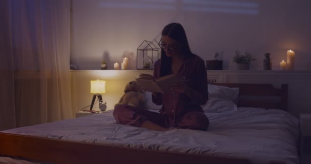 Młoda inteligentna kobieta czyta książki w łóżku późno — Wideo stockowe