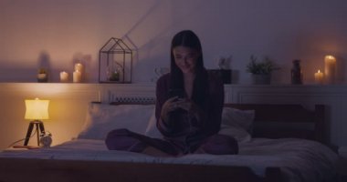 Genç bir kadın yatakta cep telefonundan aşk mesajı okuyor.