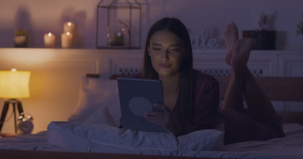 Vrouw netwerken op digitale tablet, liggend in pyjama in bed — Stockvideo