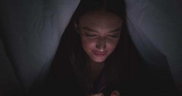 젊은 여성 웹 서핑을 하는 모습, 침대에 누워 더 베트 밑에 숨어 있는 모습 — 비디오