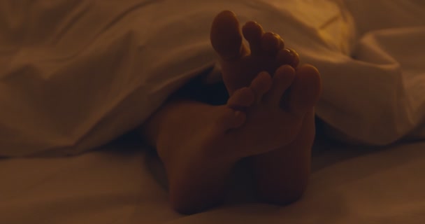 Primer plano de los pies femeninos debajo de la manta, chica durmiendo en la cama — Vídeo de stock