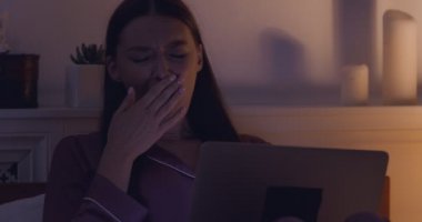 Genç yorgun kadın esniyor, geceleri laptopu kapatıyor.