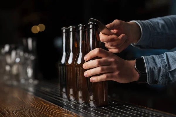 Bira festivali. Barmen gömleği bulanık arka planda bar tezgahında bira şişelerini açıyor. — Stok fotoğraf