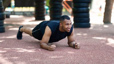 Güçlü siyah adam güneşli bir sabahta parktaki yolda dirsek kalasında duruyor.