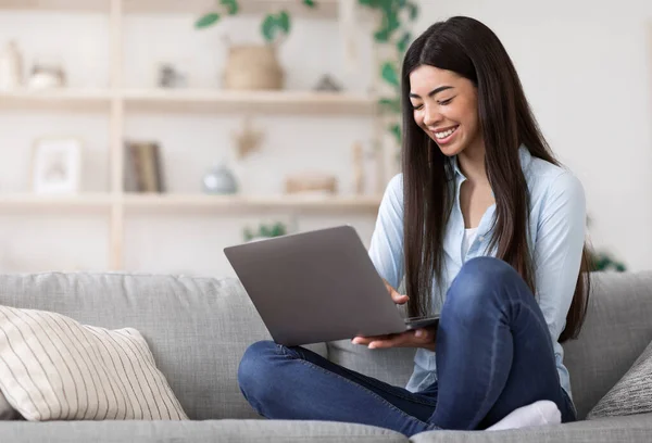 Sorrindo menina asiática trabalhando remotamente no laptop em casa, sentado no sofá — Fotografia de Stock