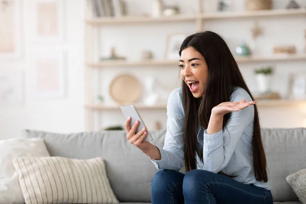 Unerwartete Botschaft. Asiatin hält Smartphone zu Hause und reagiert emotional auf Nachrichten — Stockfoto