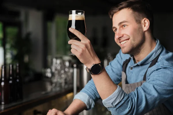 Brouwer en ambachtelijk bier. Barman bewondert donkere drank met schuim in glas — Stockfoto