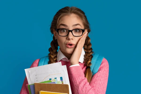 Acontece. Menina chocada adolescente em óculos pressiona a mão para bochecha e segura cadernos — Fotografia de Stock
