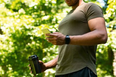 Sportif adam eğitimine ara veriyor ve parktaki akıllı telefondan internette sörf yapıyor.