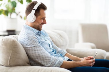 Kanepede oturmuş müzik dinleyen mutlu adam.