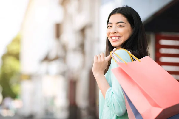 Porträtt av vacker leende asiatisk kvinna poserar med shoppingväskor på gatan — Stockfoto