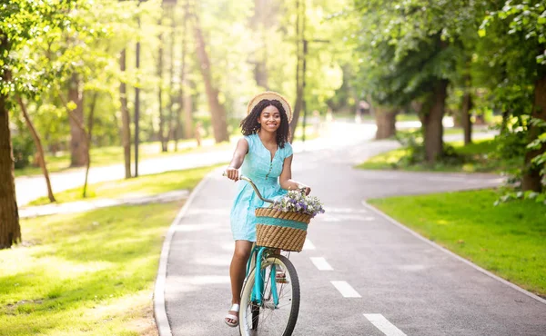 Glada svart kvinna rida cykel i parken på solig dag — Stockfoto