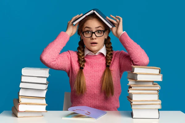 Preparation for tests. Surprised girl teenager in glasses covers her head with book