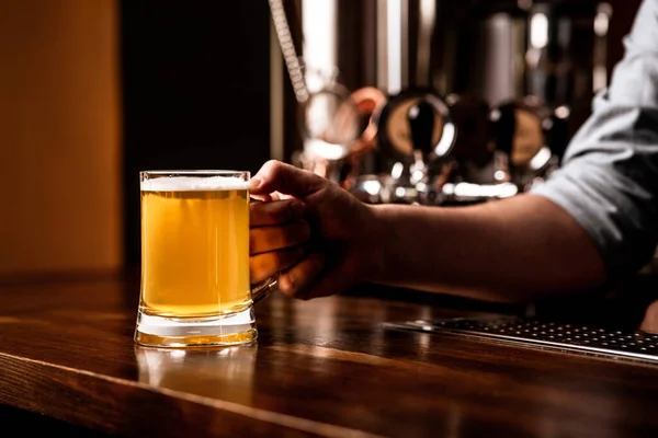 Caneca de cerveja para o cliente. Bartender coloca luz lager no contador de barra marrom de madeira — Fotografia de Stock